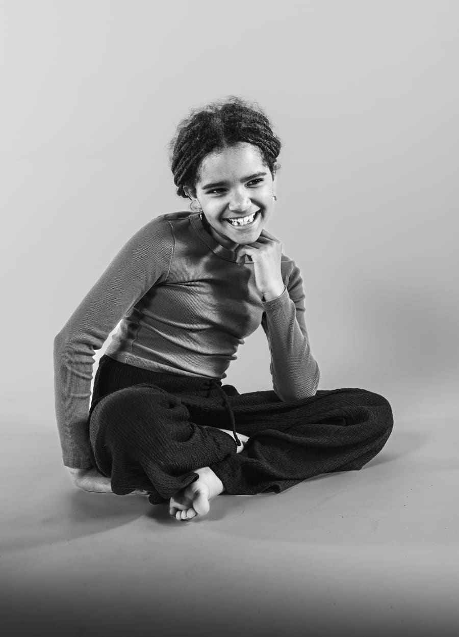 Schulfotografie: Schwarz-Weiß-Portrait eines Mädchens, das lächelnd auf dem Boden sitzt